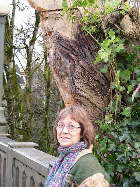  a tree carved with a pirate face is above Megan Lindholm standing on a bridge.